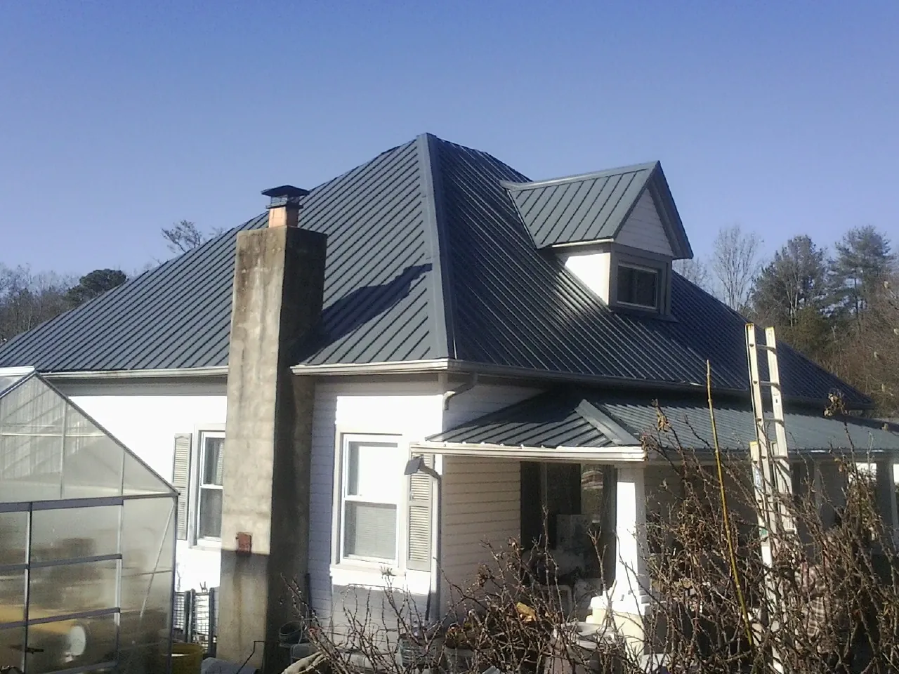 Dark blue standing seam metal roof on a white farmhouse with dormer — Slate & Tile Roof Repair by Roofing Brothers in Buxton