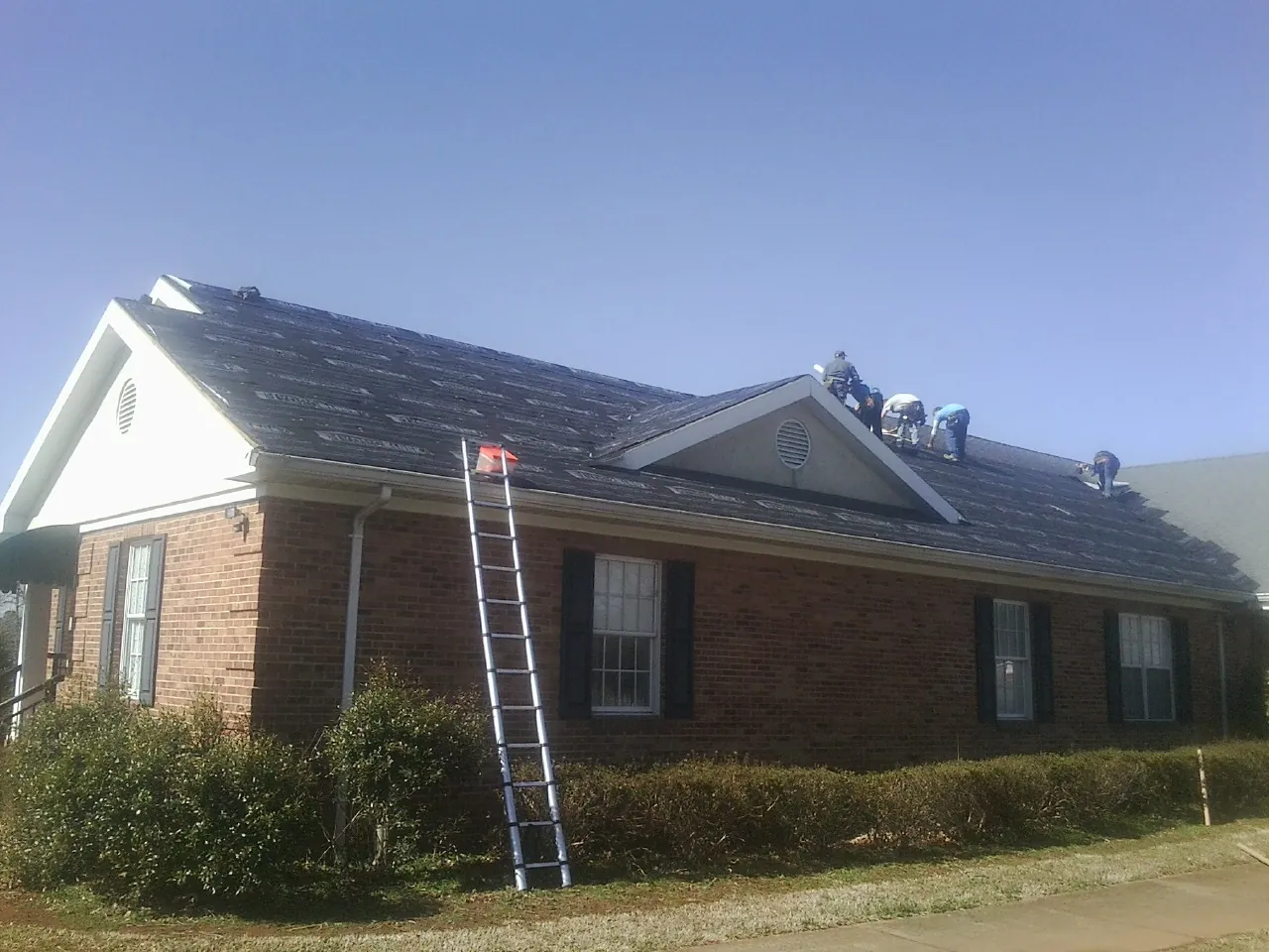 Crew tearing shingles off a brick ranch roof with a ladder set — Emergency Roof Repair work by our crew in Buxton