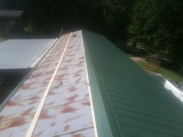 Old rusted panels beside newly installed green metal roofing — Wind Damage Roof Repair by Roofing Brothers in Buxton