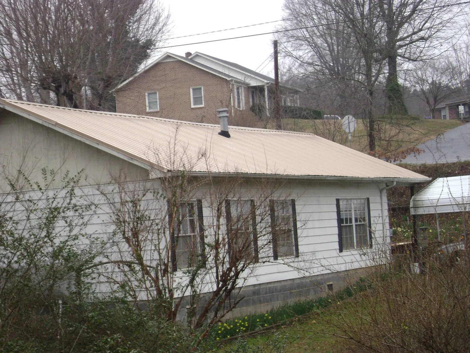 Tan metal roof on a white sided house set into a hillside — Commercial Roofing by Roofing Brothers in Buxton