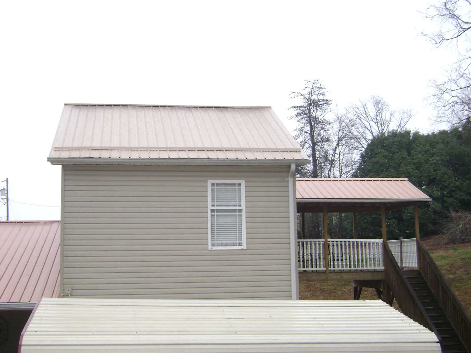 Tan metal roofs on a two story addition and attached porch, from a Roof Replacement job in Buxton